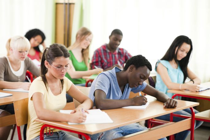 Grupo de estudiantes en clase, concentrados en sus tareas en escritorios de madera.